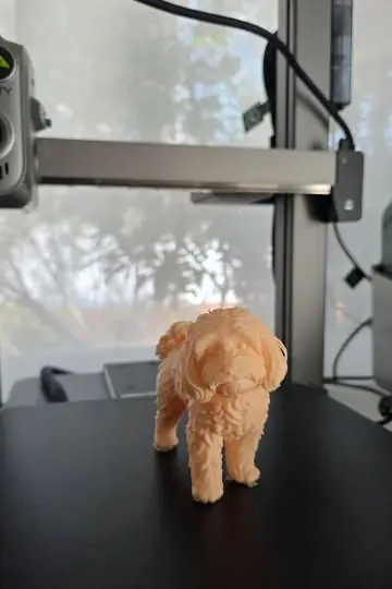 Figura 3D de una perrita maltés recién terminada de imprimir sobre la cama de la impresora 3D